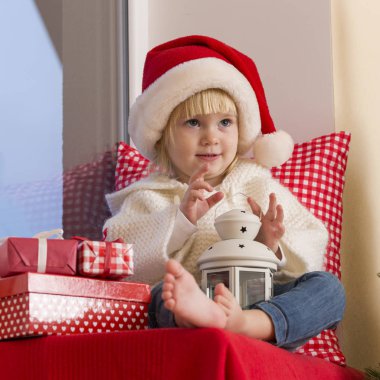 Mutlu bir aile. Bir Noel Baba'nın şapkalı küçük bir kız bir pencere pervazına penceresinde oturur ve saint için bekler.