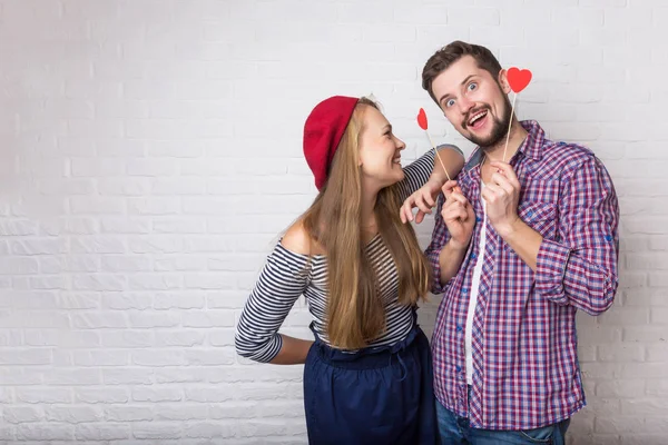 A happy funny couple in love enjoys Valentine\'s Day. A man with a beard and a woman with blond long hair. Paper red hearts. Loft style.