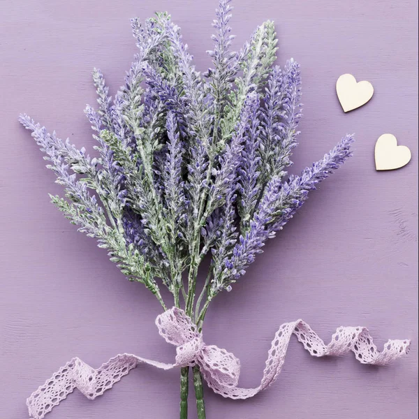 Lavender flower banded ribbon with bow on purple wooden background. Near two wooden hearts.