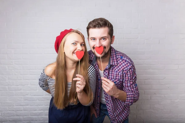 A happy funny couple in love enjoys Valentine's Day. A man with a beard and a woman with blond long hair. Paper red hearts. Loft style.