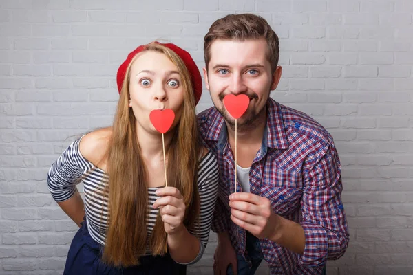 A happy funny couple in love enjoys Valentine's Day. A man with a beard and a woman with blond long hair. Paper red hearts. Loft style.