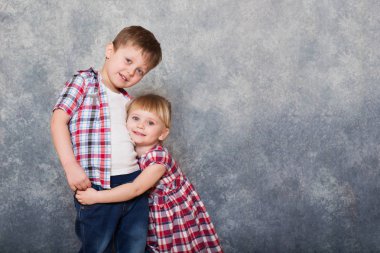 İki çocuk: bir erkek ve bir kız kılığında kırmızı kareli elbiseler içinde birbirlerine sarılma, gülen ve görüntüleyiciyi arıyor. Kardeşin ilişkileri.