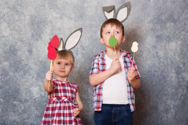 İki çocuk, bir kız ve çocuk ile Paskalya tavşan kulaklar kafa gülmek ve oyun. Ellerindeki karton yapılmış renkli Paskalya yumurtaları tutuyorlar. Kopya alanı.