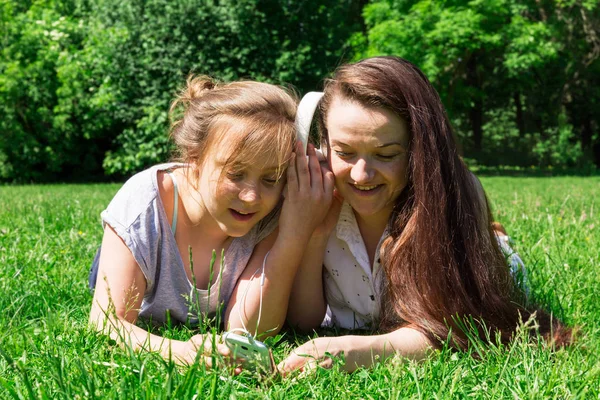 Two girls: younger and older, listen to music over the phone. Spending time with a friend in the park.