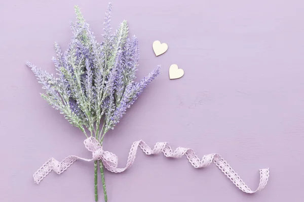 Lavender flower banded ribbon with bow on purple wooden background. Near two wooden hearts.