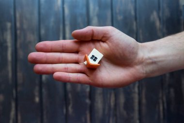 Küçük heykelcik, bir oyuncak, bir evin bir model üzerinde açık bir erkek el yalan söylüyor. Tahta geri zemin. Üstten görünüm, kopya alanı.