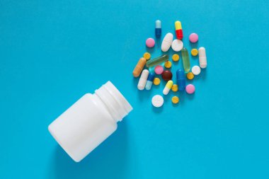Boş bir mavi arka plan üzerinde beyaz bir plastik şişe renkli farklı tablet döktüm. Kopya alanı. 