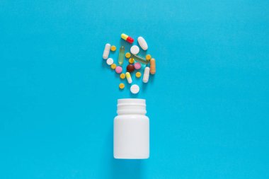 Boş bir mavi arka plan üzerinde beyaz bir plastik şişe renkli farklı tablet döktüm. Kopya alanı. 