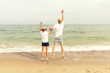 İki genç: bir kız ve bir erkek sarışın saçlı giymiş beyaz T-shirt ve şort bir deniz sahilde elele atlama. Kopya alanı.