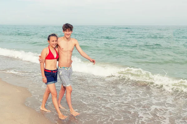 二十代の若者 少女とブロンドの髪を持つ少年が服を水着姿で歩く海のビーチで視聴者へ帰国 — ストック写真