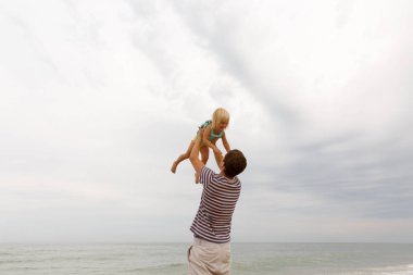 Babası yukarı doğru gülen çocuk atar. Sahilde bir aile tatili. Kopya alanı.
