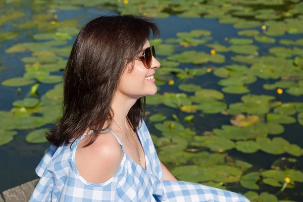 Güneşli bir günde Köprü Nehri yakınında güneş gözlüklü genç kadın oturur.