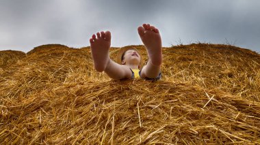 Küçük güzel çocuk bir sarı tişört ve kot şort giymiş ve modern şapka bir haystack bir yaz günü oturur. Hasat.