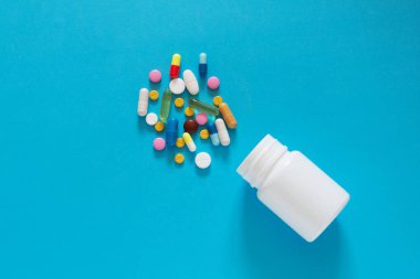 Boş bir mavi arka plan üzerinde beyaz bir plastik şişe renkli farklı tablet döktüm. Kopya alanı. 