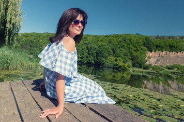 Güneşli bir günde Köprü Nehri yakınında güneş gözlüklü genç kadın oturur.