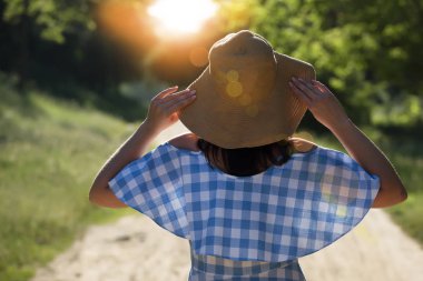 Güneşte rahatlatır bir hasır şapkalı kadın arkadan görünüm. Siluet, güneş ışıkları.