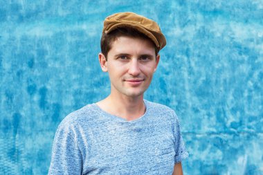 Bir mavi gömlek ve mavi bir arka plan üzerine şapka genç bir adam portresi. Kopya alanı.