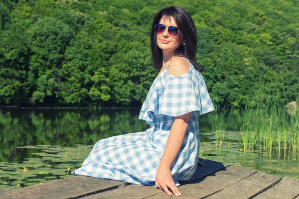 Güneşli bir günde Köprü Nehri yakınında güneş gözlüklü genç kadın oturur.