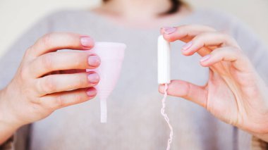Tampon veya adet Kupası? Fem Kupası ve tampon tutan kadınsı bir el. Seçici odak.