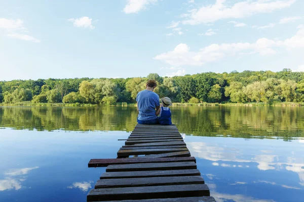 Papá y una niña pequeña en Dungarees relajarse en el río. Vista trasera , — Foto de Stock