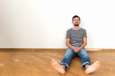 Genç bir adam, yeni bir daire içinde katta oturuyor. Boşluk, beyaz duvar kopyalama.