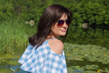 Güneşli bir günde Köprü Nehri yakınında güneş gözlüklü genç kadın oturur.