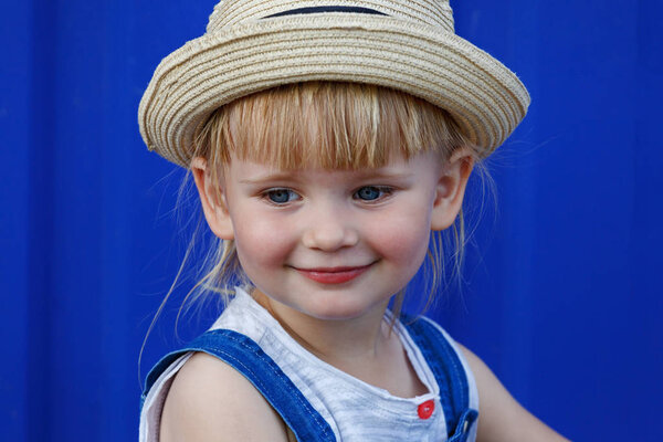 Portrait of a little girl in a straw hat. She looks at the viewer and smiles at the camera.