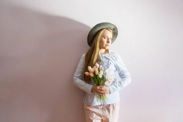 溶存長い金髪 彼女の頭の上にフェルト帽子の美しい少女は 彼女の手で晴れた日に春の花を保持します 女性の日 — ストック写真