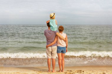 Mutlu bir aile! Baba, anne ve kızı deniz kıyısı üzerinde duruyor. Arkadan görünüm.
