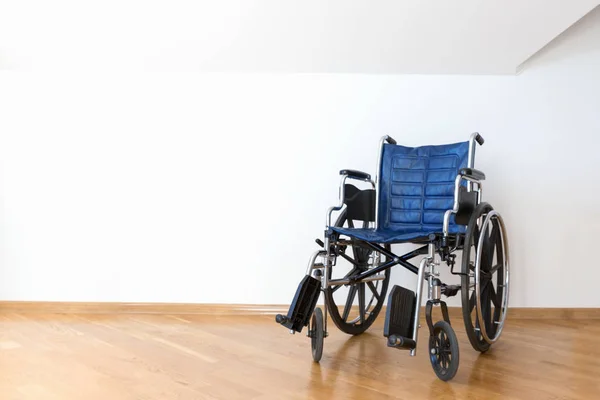 Empty blue wheelchair in a white room.