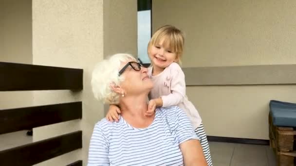 Kleine süße Enkelin umarmt Großmutter und sie lachen zusammen. Zeitlupe, Nahaufnahme. — Stockvideo