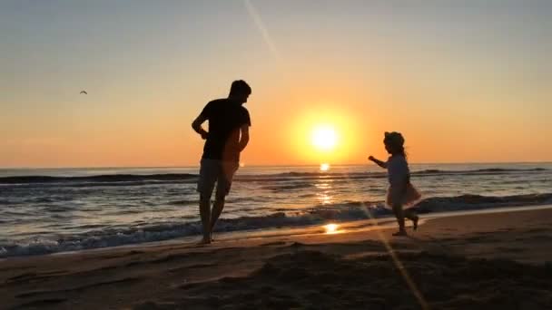 Vater und Tochter laufen bei Sonnenuntergang am Strand entlang. — Stockvideo