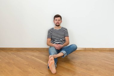 Genç bir adam, yeni bir daire içinde katta oturuyor. Boşluk, beyaz duvar kopyalama.