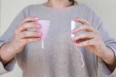 Tampon veya adet Kupası? Fem Kupası ve tampon tutan kadınsı bir el. Seçici odak.