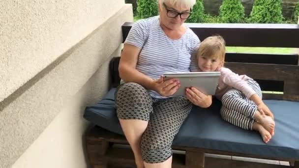 Grand-mère et petite-fille assises sur la terrasse et utilisant la tablette . — Video