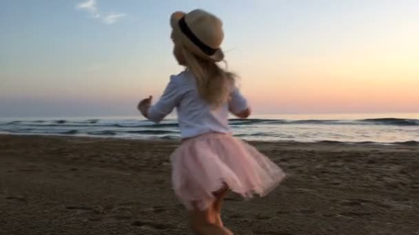 En liten flicka springer längs stranden vid solnedgången. — Stockvideo
