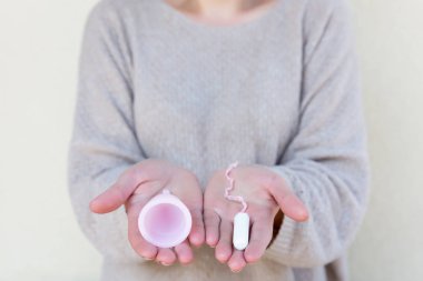 Tampon veya adet Kupası? Fem Kupası ve tampon tutan kadınsı bir el. Seçici odak.