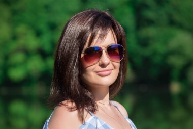 Kareli desen elbise giymiş genç kadın portresi kapatın. Orman ve göl arka plan. 