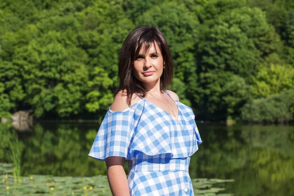 Portrait of young woman with dark hair whose stands of a forest and lake backgraund. Sunny summer day