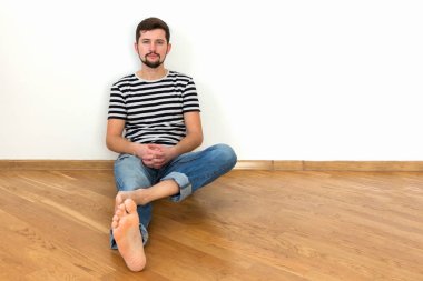 Genç bir adam, yeni bir daire içinde katta oturuyor. Boşluk, beyaz duvar kopyalama.