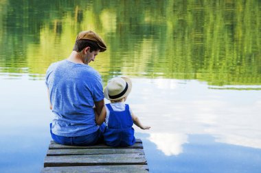Baba ve kaba pamuklu Tulum içinde küçük bir kız nehirde rahatlayın. Arkadan görünüm, kopya alanı.
