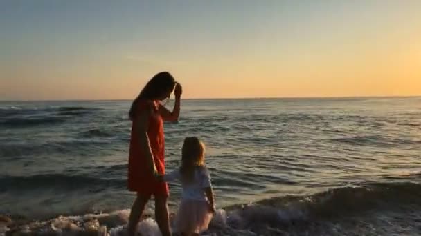 Petite fille et jeune femme marchant le long de la plage . — Video