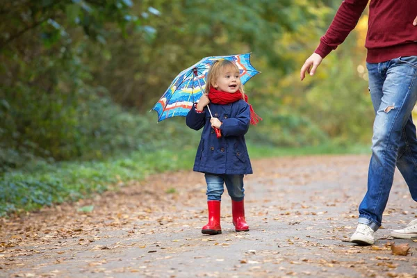 A small girl dressed in rubber boots and raincoats, holds an umbrella, laughs and runs through an autumn park.