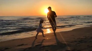 Baba ve kızı gün doğumunda plajda koşuyorlar..