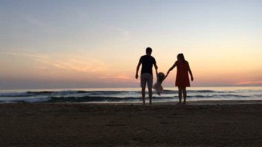 Anne ve baba sahilde çocuk sallıyor. Anne ve baba gün batımında çocuğu sahilde sallıyor..