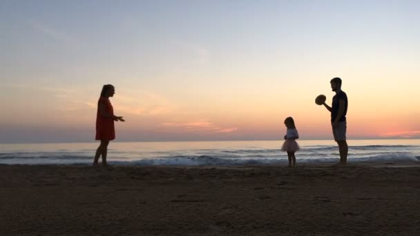 Meisje loopt tussen haar ouders langs het strand bij zonsondergang. — Stockvideo