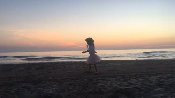 Mała dziewczynka tańczy na plaży o zachodzie słońca. — Wideo stockowe