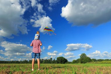 Baba ve kızı tarlada uçurtma uçuruyorlar.