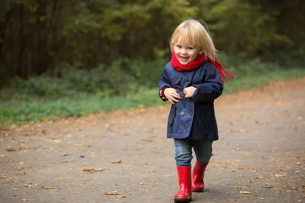 Happy autumn. Little girl laughs and runs in galoshes through th