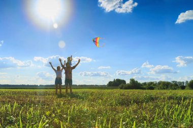 Anne, baba ve kızı tarlada uçurtma uçuruyorlar. Fron